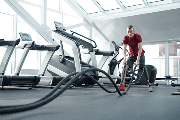 Man with prosthetic leg using ropes at gym