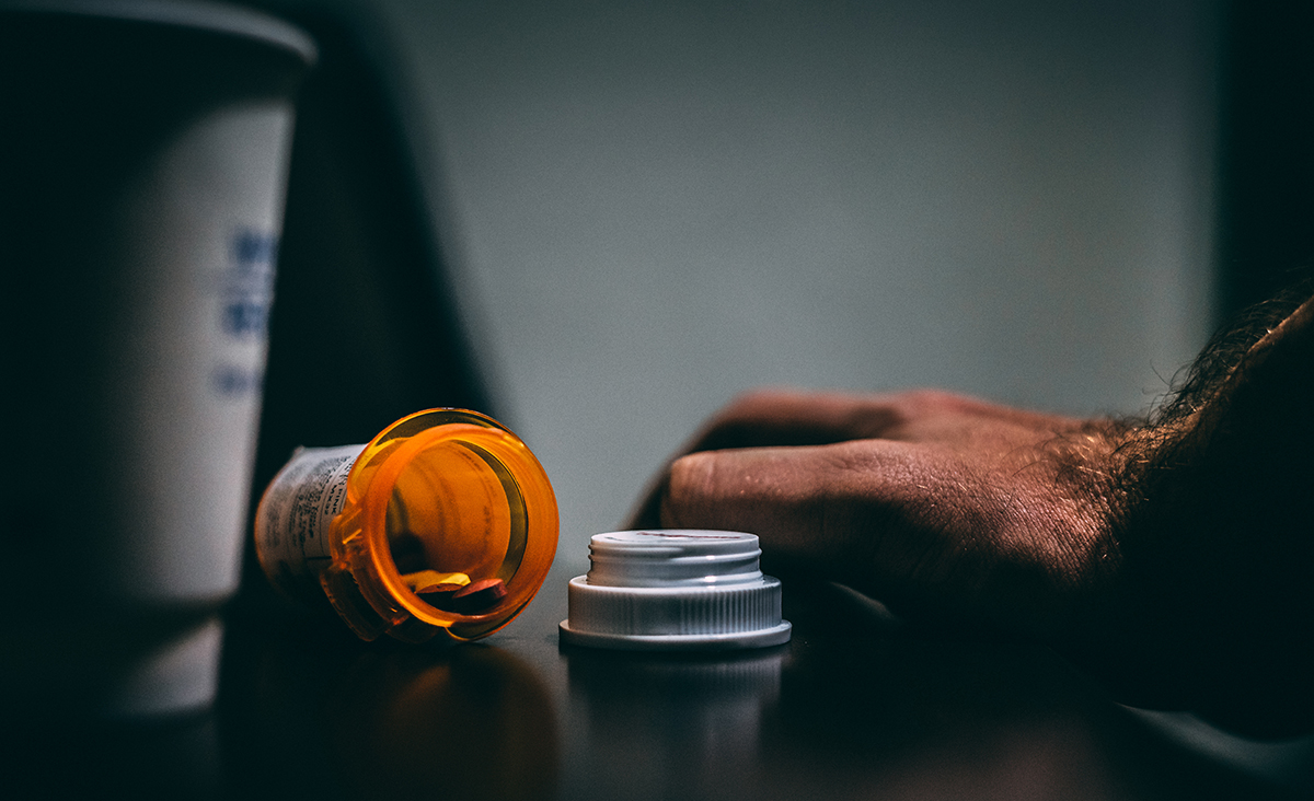 Hand next to open bottle of pills