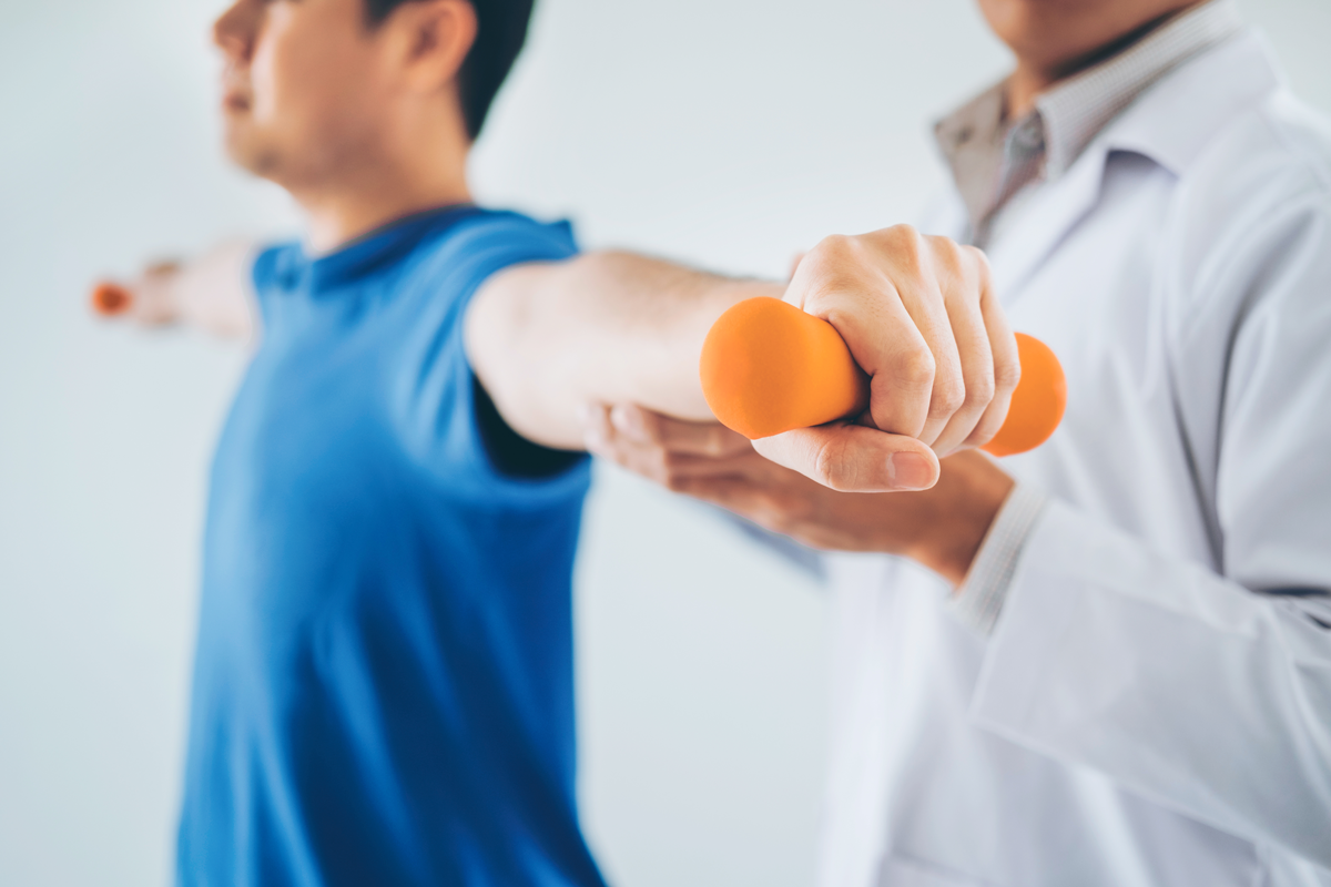 Physical therapist assisting young man lift dumbbell 
