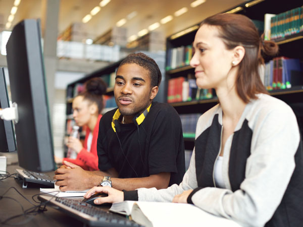 A female is tutoring a male child in the library